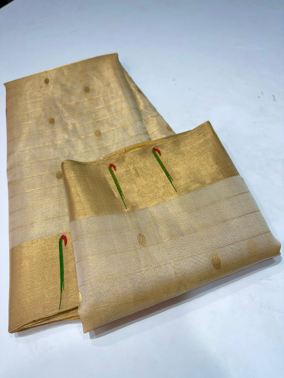 Folded champagne gold Chanderi Katan silk saree with traditional kinar butti and small zari dots.